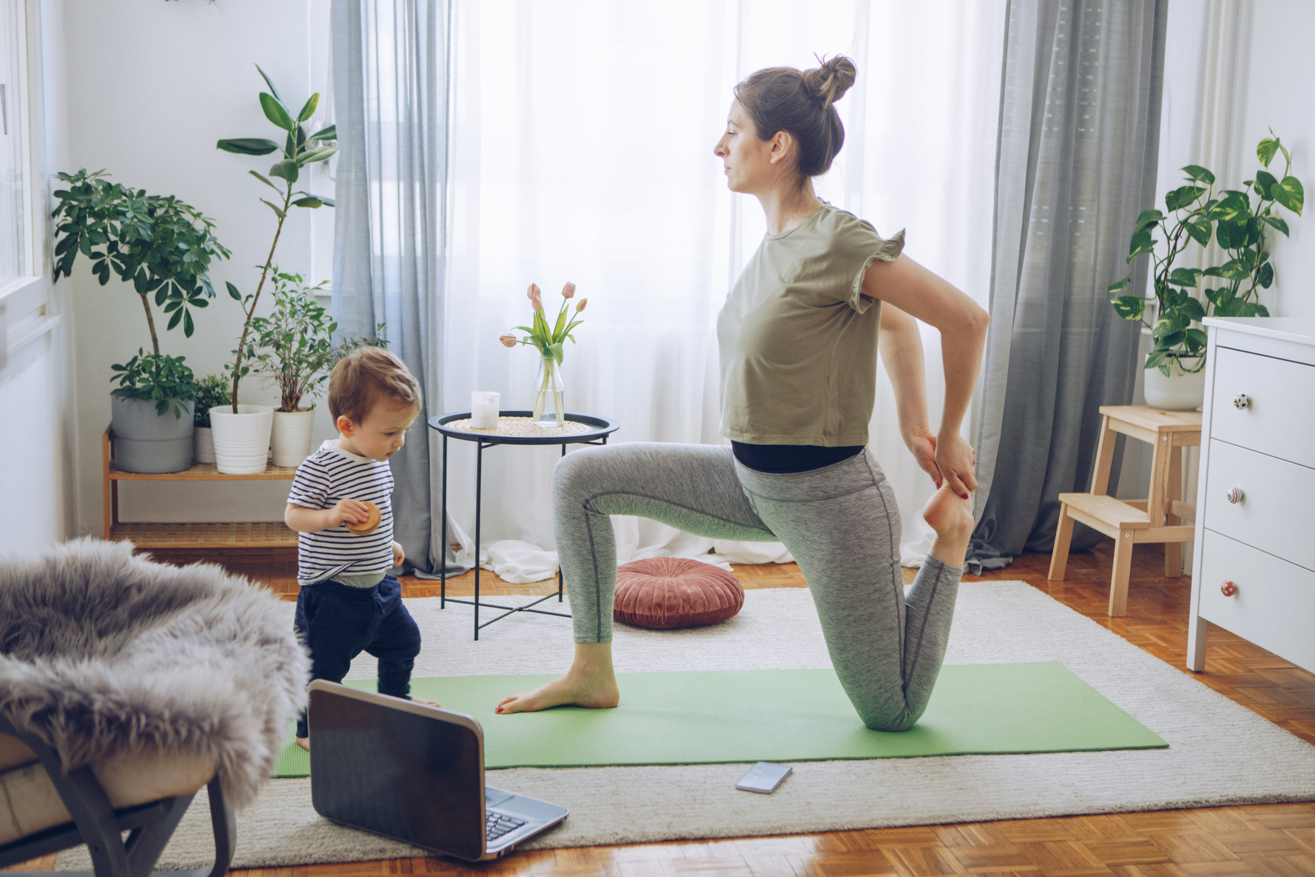 Women exercise yoga while her baby son exploring living room