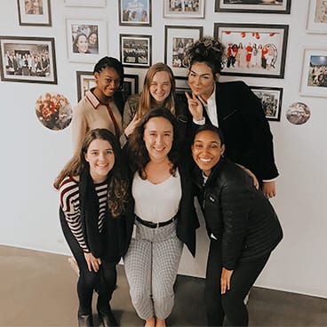 Six women standing in front of framed photos