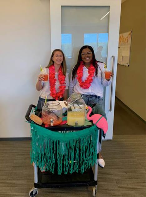 Two women holding drinks from bar cart inside the office