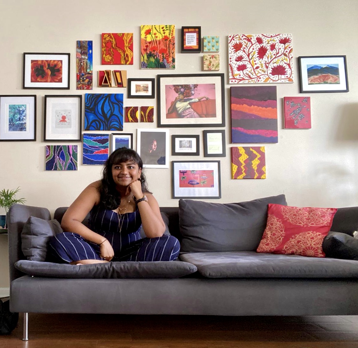 Woman smiling, sitting on on a couch with wall of art behind her
