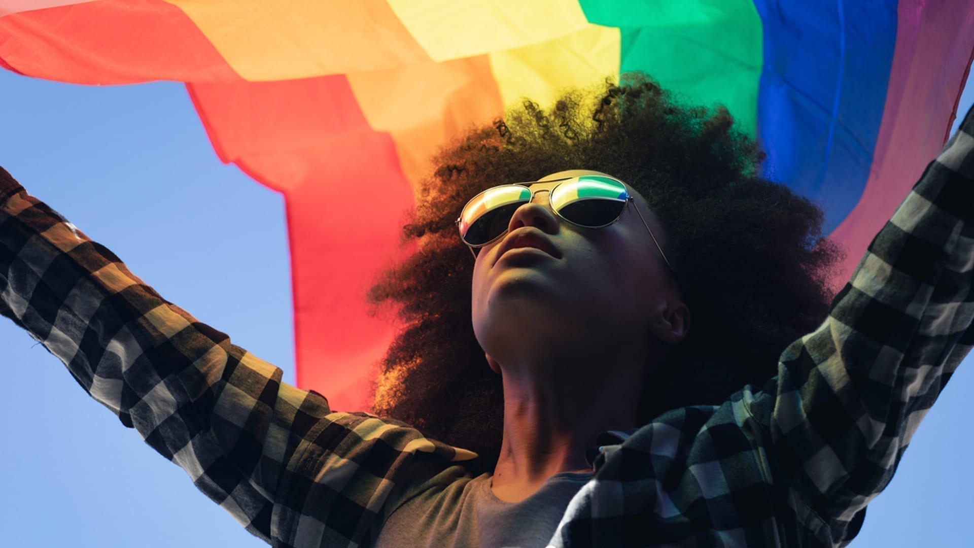 Pride Month 2021 - Evolving the Celebration - photo of black woman holding pride flag over her head