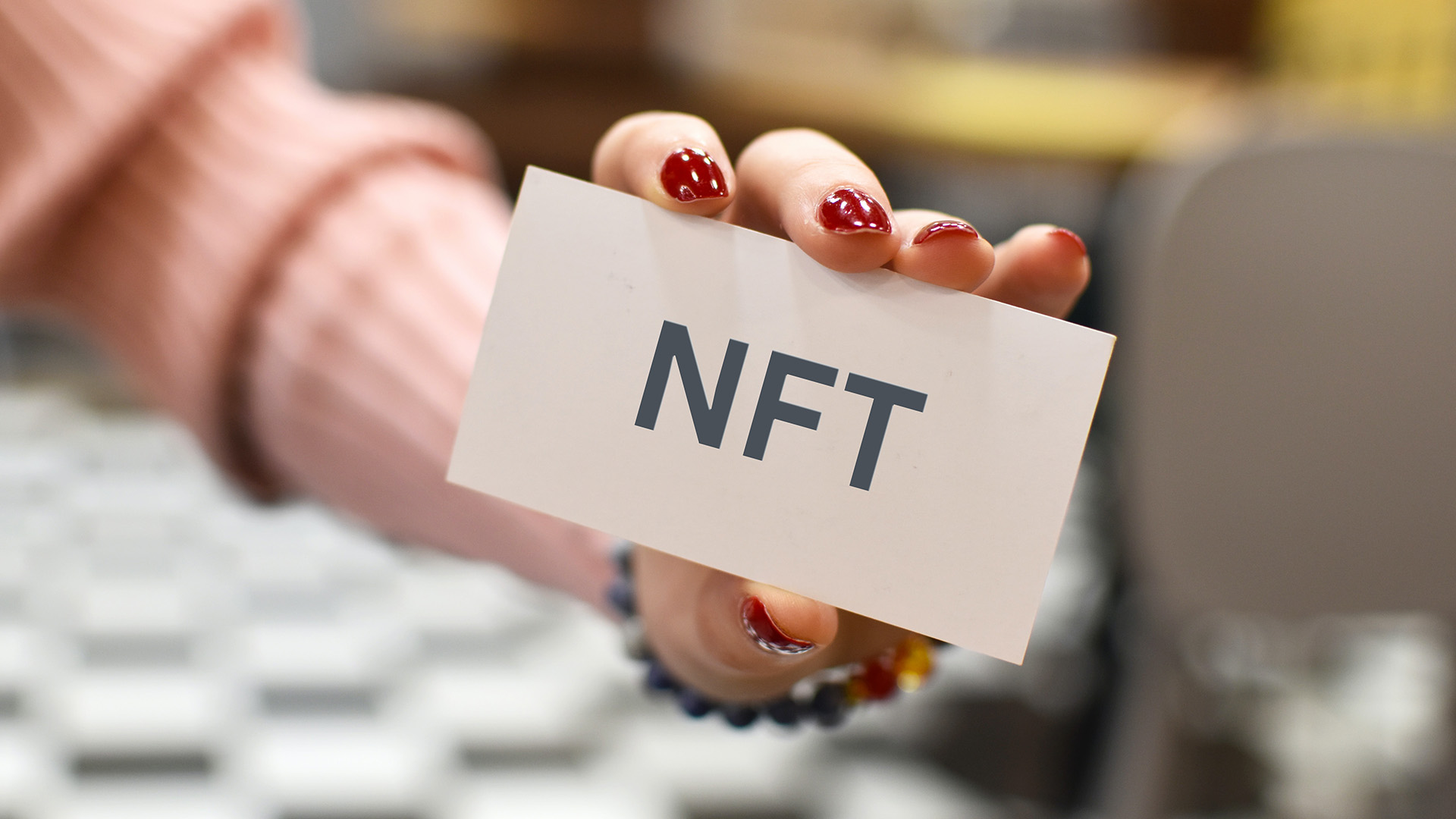 Hand holding and showing a card that says "NFT" on it. 