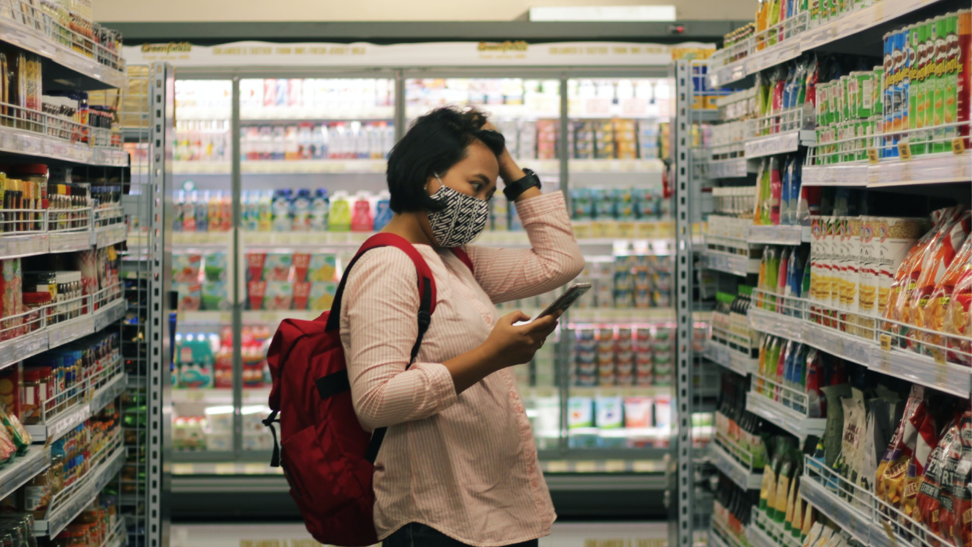 Woman holding phone in one hand and grasping her hair with other hand appears stressed looking at grocery store shelves
