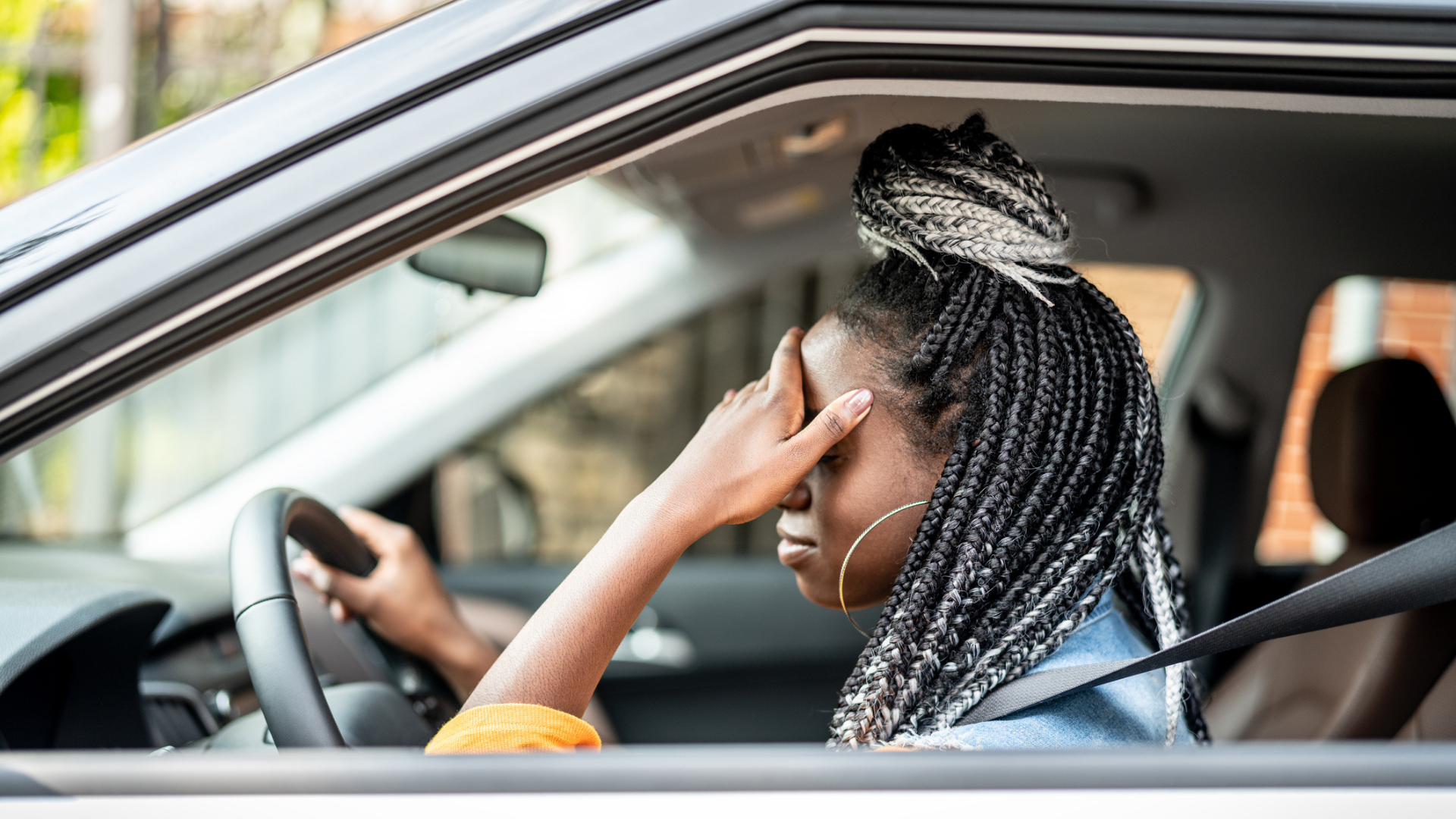 photo of a women sitting in a car in traffic, with hand on head looking frustrated
