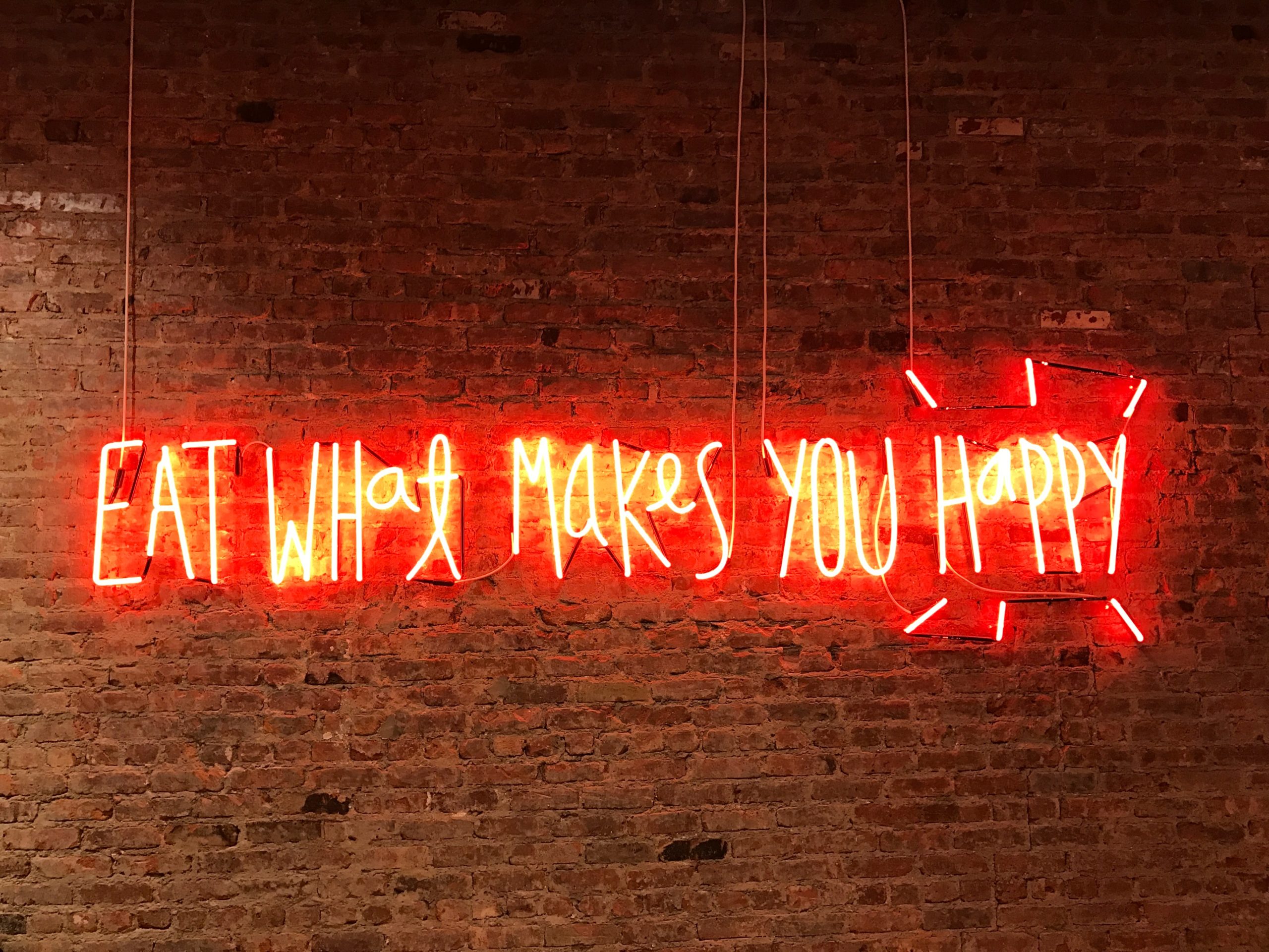 Neon sign that says “eat what makes you happy.” 