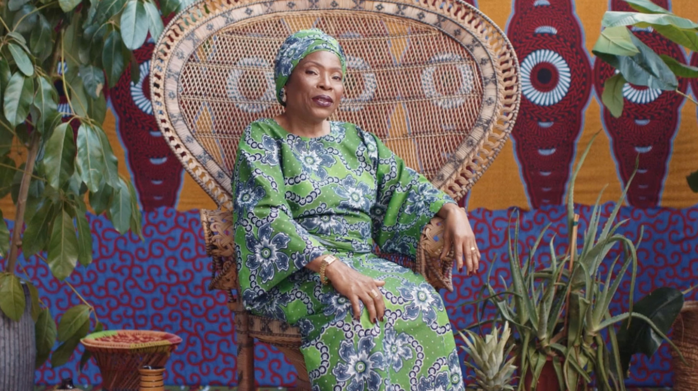 person sitting in large chair with plants on both sides and a colorful wall behind them.