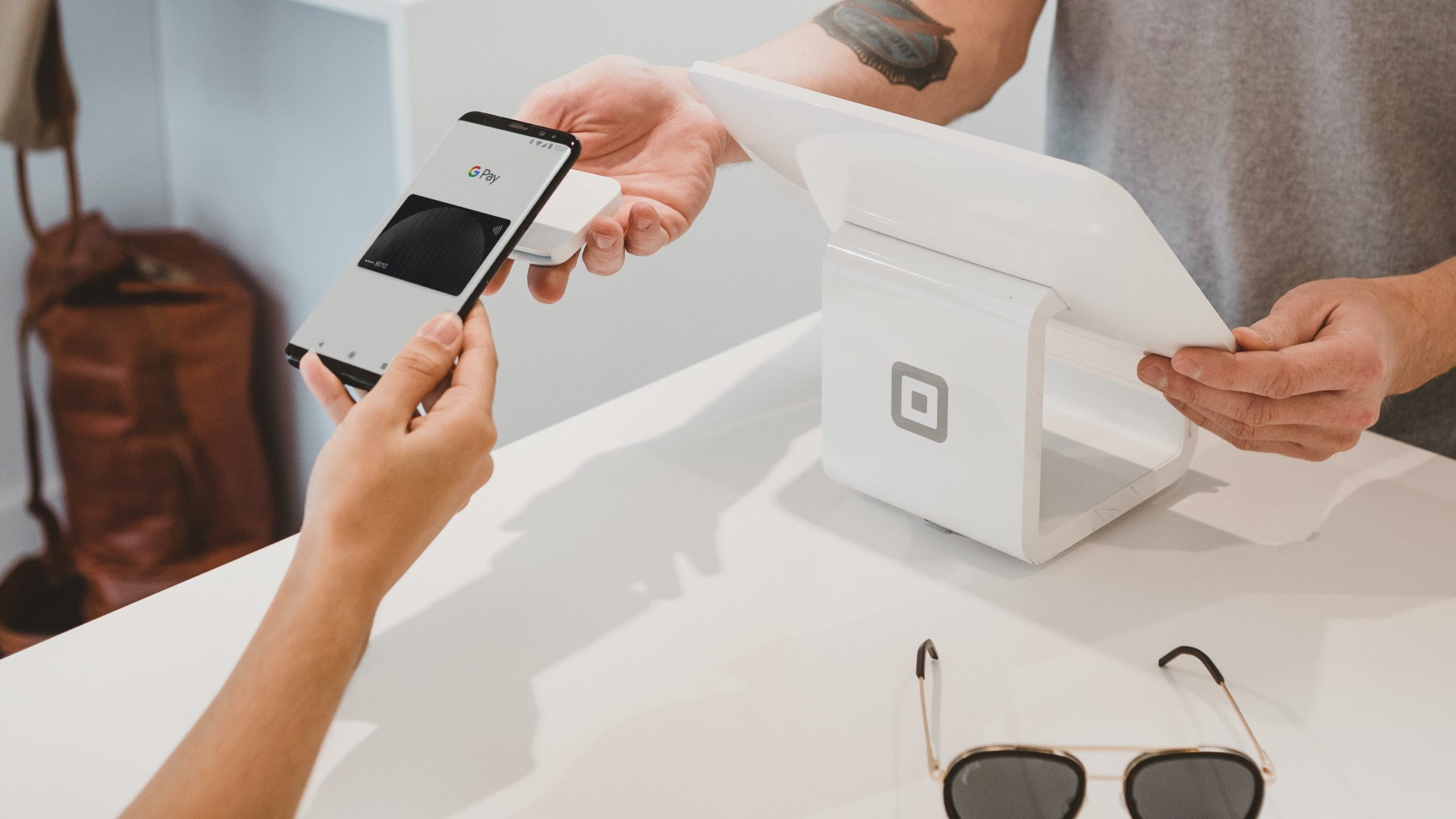 Over shopping counter hand holds smart phone tapping it on card reader for contactless and chip payments.